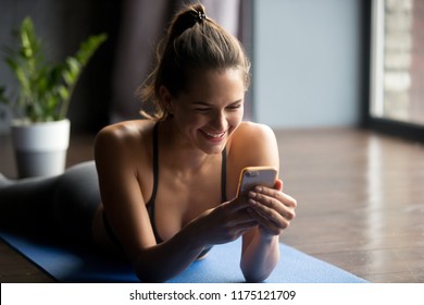 Young sporty woman after practicing yoga, break in doing exercise, relaxing on yoga mat, texting on the cell phone, holding smartphone, friendly smiling reading message, indoor close up, yoga studio - Powered by Shutterstock