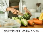 Young sporty woman chopping fresh broccoli on cutting board preparing containers of healthy food. Healthy eating and a balanced lifestyle concept.