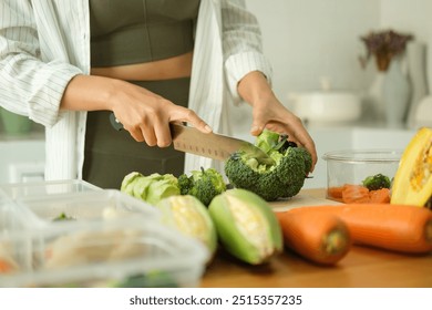 Young sporty woman chopping fresh broccoli on cutting board preparing containers of healthy food. Healthy eating and a balanced lifestyle concept.