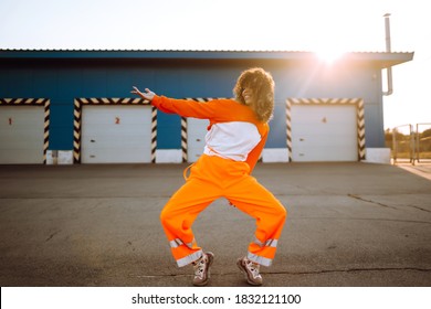 Young Sporty Woman Dancer Dancing In The Street At Sunset. African American Woman In An Orange Suit Showing Some Moves. Sport, Dancing And Urban Culture Concept.