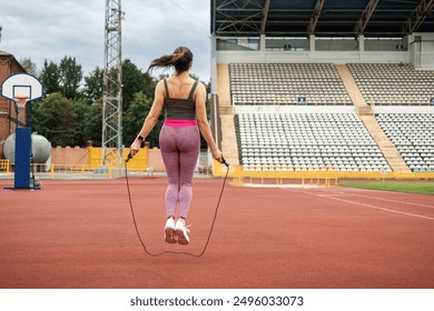 A young sporty woman doing her morning workout, skipping rope on the stadium, outdoors, back view. - Powered by Shutterstock