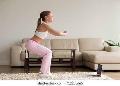 Young Sporty Woman Doing Two-leg Deep Squat Morning Exercise Standing In Living Room, Teen Girl Burning Fat Calories With Online Fitness Training Help Crouching For Buttocks Lift At Home, Side View