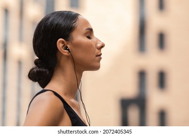 Young Sporty Woman In Earphones Listening Music With Closed Eyes Outdoors, Calm Millennial Lady Relaxing After Training Outside, Enjoying Favorite Playlist, Side View Shot With Copy Space - Powered by Shutterstock