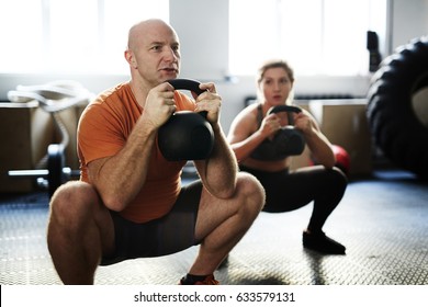 Young Sporty Woman And Middle-aged Bodybuilder Doing Kettlebell Squat Exercise During Intensive Training In Gym