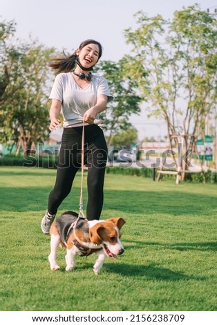 Young sporty woman playing with her beagle dog walking with dog leash at park with happy moment at evening time