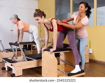 Young sporty woman practicing Pilates system exercises on wunda chair under guidance of positive qualified Hispanic female trainer - Powered by Shutterstock