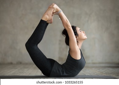 Young sporty woman practicing yoga, doing Dhanurasana exercise, Bow pose, working out, wearing sportswear, black pants and top, indoor full length, gray wall in yoga studio - Powered by Shutterstock