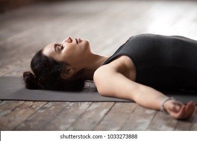 Young sporty woman practicing yoga, lying with eyes closed in Dead Body or Corpse pose, Savasana exercise, working out wearing sportswear top, resting after yoga, indoor close up photo, studio - Powered by Shutterstock