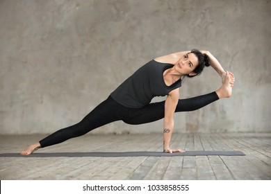 Young Sporty Woman Practicing Yoga, Doing Visvamitrasana Exercise, Arm Balance Pose, Working Out, Wearing Sportswear, Black Pants And Top, Indoor Full Length, Gray Wall In Yoga Studio