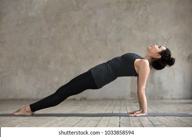 Young sporty woman practicing yoga, doing Purvottanasana exercise, Upward Plank pose, working out, wearing sportswear, black pants and top, indoor full length, gray wall in yoga studio - Powered by Shutterstock