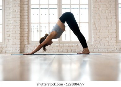 Young Sporty Woman Practicing Yoga, Doing Downward Facing Dog Exercise, Adho Mukha Svanasana Pose, Working Out, Wearing Sportswear, Pants And Top, Indoor Full Length, White Yoga Studio