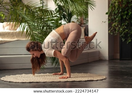 Young sporty woman practicing yoga at home,doing Crane Pose,Bakasana.Relaxation and meditation.Wellness,wellbeing,mental health concept.