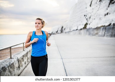 Young Sporty Woman Runner With Earphones Running On The Beach Outside.