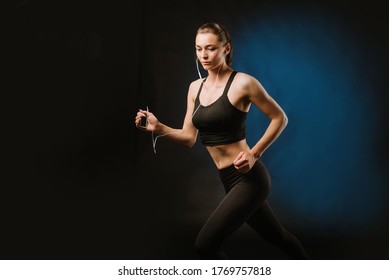 Young sporty woman running with earphones on black background