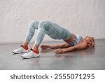 Young sporty woman in sportswear, leggings and bra practicing yoga, beautiful girl doing Glute Bridge exercise, dvi pada pithasana pose, working out in yoga studio.