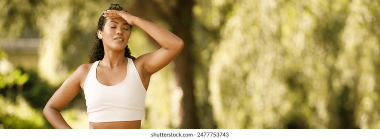 Young sporty woman struggles with exhaustion during her marathon training, jogging outside in green park on summer day. She touches her head, feeling unwell and dizzy outdoors, copy space - Powered by Shutterstock