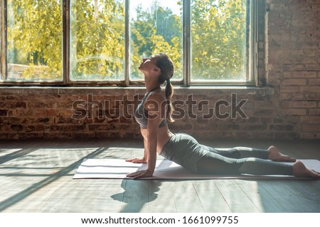 Young sporty woman trainer do practice individual hatha yoga instructor training Bhujangasana pose high cobra posture prone backbend position mat modern gym fitness workout healthy lifestyle concept.