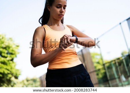 Young sporty woman training in the park. Beautiful woman in sportswear using smartwatch	