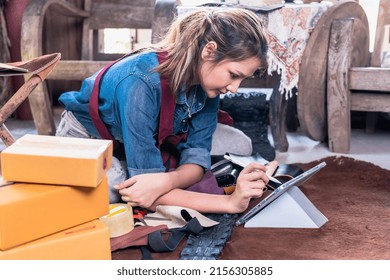 Young Startup Asian Leather Worker Woman Looking At IPad Checking  Online Orders To Prepare The Packages For Customers In Leather Art And Craft Shop 