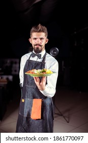 Young Steward Helpfully Holds Plate With Prepared Dish At A Festive Event.