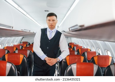 Young steward in uniform on the work in the passanger airplane. - Shutterstock ID 2136435321