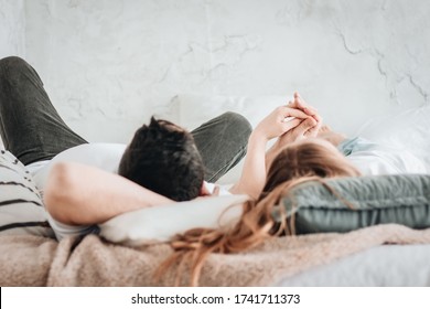 Young straight couple laying on backs on bed holding hands. side view 
