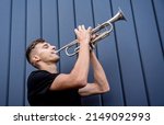 Young street musician playing the trumpet near the big blue wall