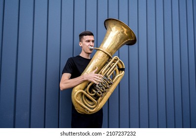 Young street musician playing the tuba near the big blue wall - Shutterstock ID 2107237232