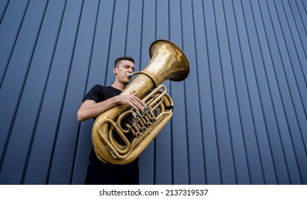 Young street musician playing the tuba near the big blue wall