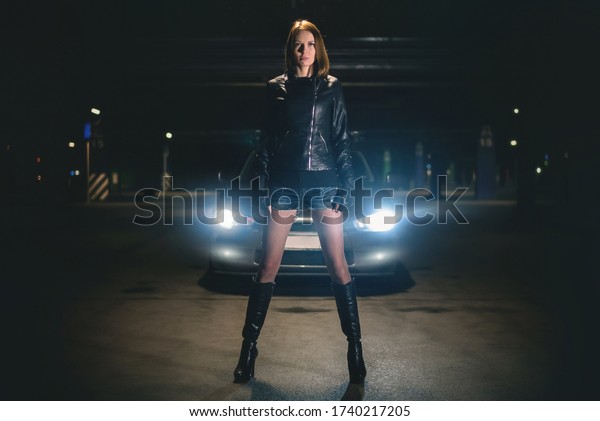A young street racer woman is standing at night\
parking concept.
