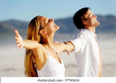 Young Stress Free Couple Enjoy The Summer Sun On The Beach. Arms Out, Heads Back And Carefree Attitudes.