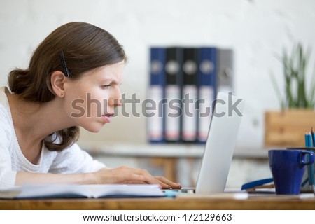 Young stressed businesswoman sitting with laptop and looking at screen with concerned facial expression. Surprised and focused business person staring at laptop computer screen worried and interested