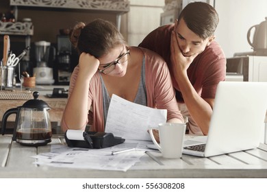 Young stressed Caucasian couple facing financials troubles, sitting at kitchen table with papers, calculator and laptop computer and reading document from bank, looking frustrated and unhappy - Shutterstock ID 556308208