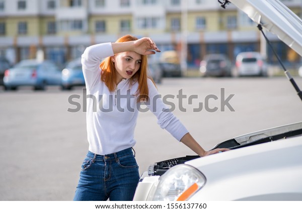 Young stressed woman driver standing near broked\
car with open hood.