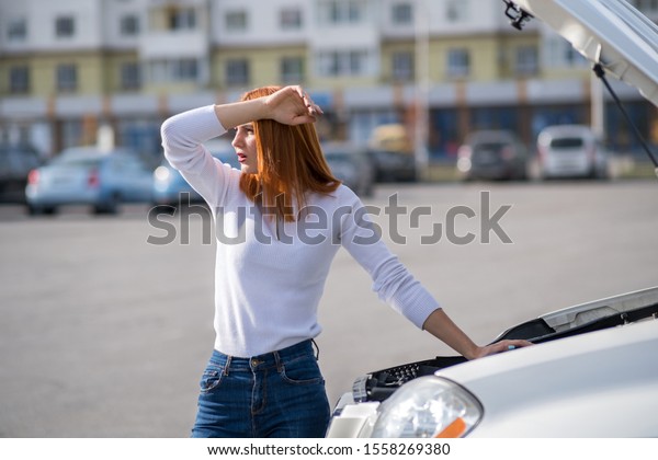 Young stressed woman driver standing near broked
car with open hood.