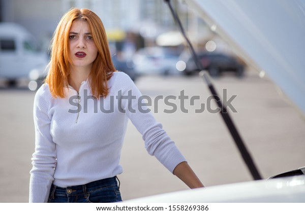 Young stressed woman driver standing near broked
car with open hood.