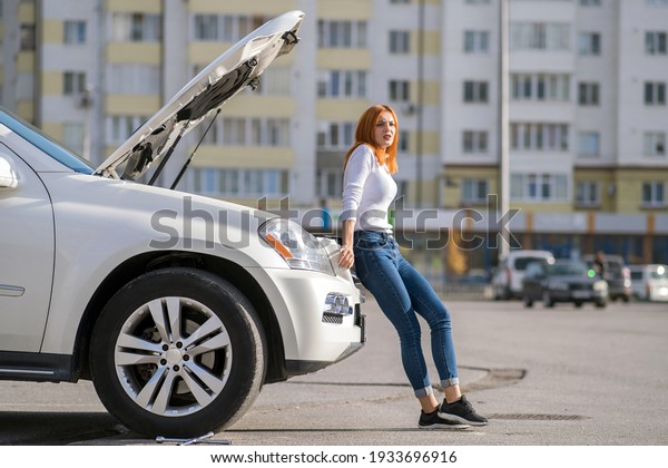 Young stressed woman driver standing near broked\
car with open hood.