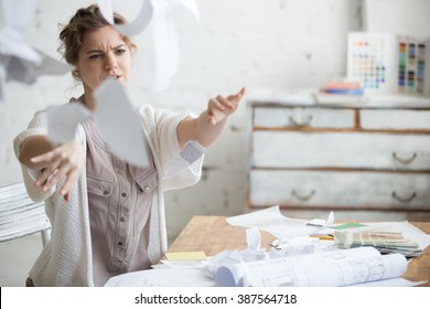 Young Stressed Woman Sitting At Desk In A Little Office Or Home Mad At Work, Ripping Documents With Frustrated Facial Expression. Throwing Around Scraps Of Paper. Negative Human Emotions