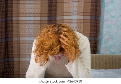 Young stressed woman sitting on the bed and hold her hand on her own head