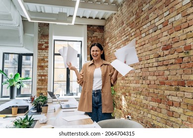 Young Stressed Woman Standing At The Desk In A Little Office Mad At Work, Screaming With Documents With Frustrated Facial Expression. Scraps Of Paper Around. Negative Human Emotions 