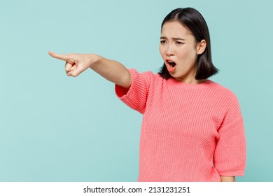 Young strict angry sad woman of Asian ethnicity 20s wearing pink sweater point index finger aside scream isolated on pastel plain light blue color background studio portrait. People lifestyle concept