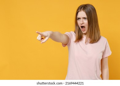 Young strict serious angry indignant leader caucasian woman 20s wearing casual basic pastel pink t-shirt point index finger aside screaming shout isolated on yellow color background studio portrait