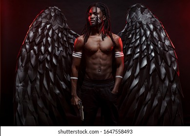 young strong black angel with cool wings, stand posing at camera. man fall from heaven, angel with muscular body gained freedom. fantasy concept, unusual creative photoshot