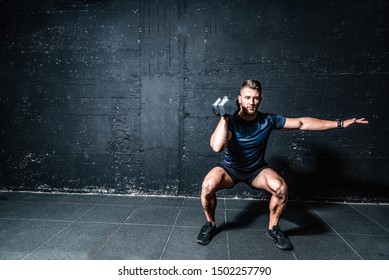 Young strong fit muscular sweaty man with big muscles strength cross workout training with dumbbells weights in the gym dark image with shadows real people