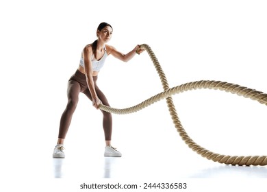 Young strong fit woman doing exercises with battle ropes at gym against white studio background. Concept of sport and recreation, movement, self care, action, energy, dynamic. Ad - Powered by Shutterstock