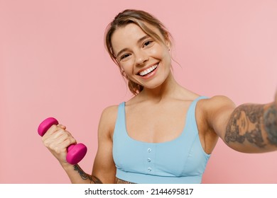 Young strong fitness trainer instructor woman wear blue tracksuit spend time in home gym hold female dumbbells do selfie shot on mobile phone isolated on plain pink background. Workout sport concept. - Powered by Shutterstock