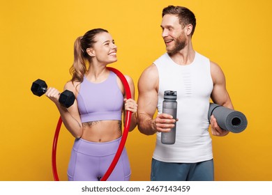 Young strong fitness trainer instructor sporty two man woman wearing blue clothes spend time in home gym hold yoga mat dumbbells hula hup isolated on plain yellow background. Workout sport fit concept - Powered by Shutterstock