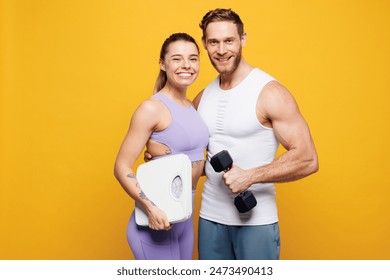 Young strong fitness trainer instructor sporty two man woman wear blue clothes spend time in home gym hold in hand scales dumbbell hug isolated on plain yellow background. Workout sport fit concept - Powered by Shutterstock