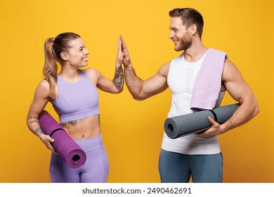 Young strong fitness trainer instructor sporty two man woman wear blue clothes spend time in home gym hold yoga mat caremat give high five isolated on plain yellow background Workout sport fit concept - Powered by Shutterstock