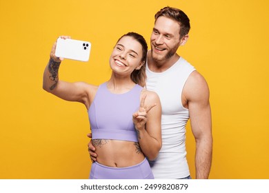 Young strong fitness trainer instructor sporty two man woman wear blue clothes spend time in home gym do selfie shot on mobile cell phone isolated on plain yellow background. Workout sport fit concept - Powered by Shutterstock